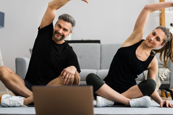 Two people stretching at home in front of a laptop