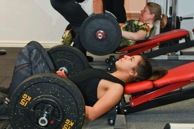 Two women lifting weights on benches in the gym