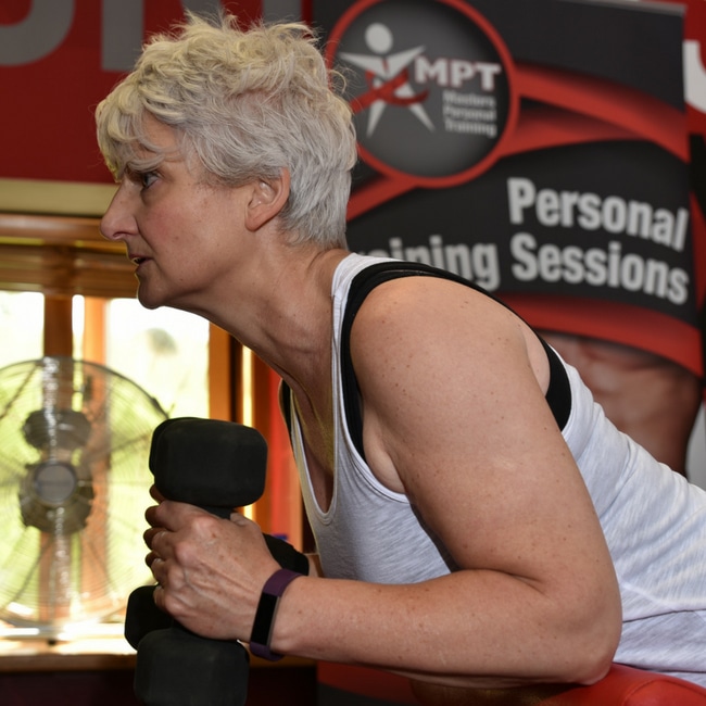 A member training with dumbbells in front of a personal training banner