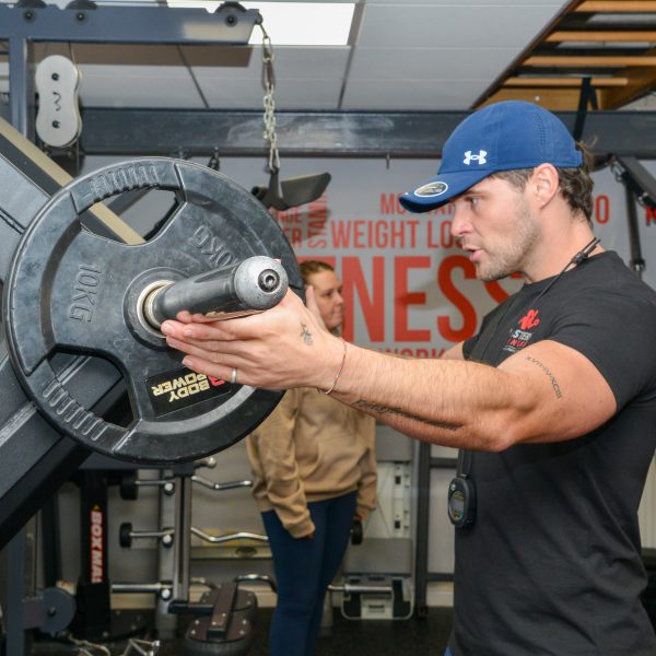 A trainer loading a weight plate while coaching a client