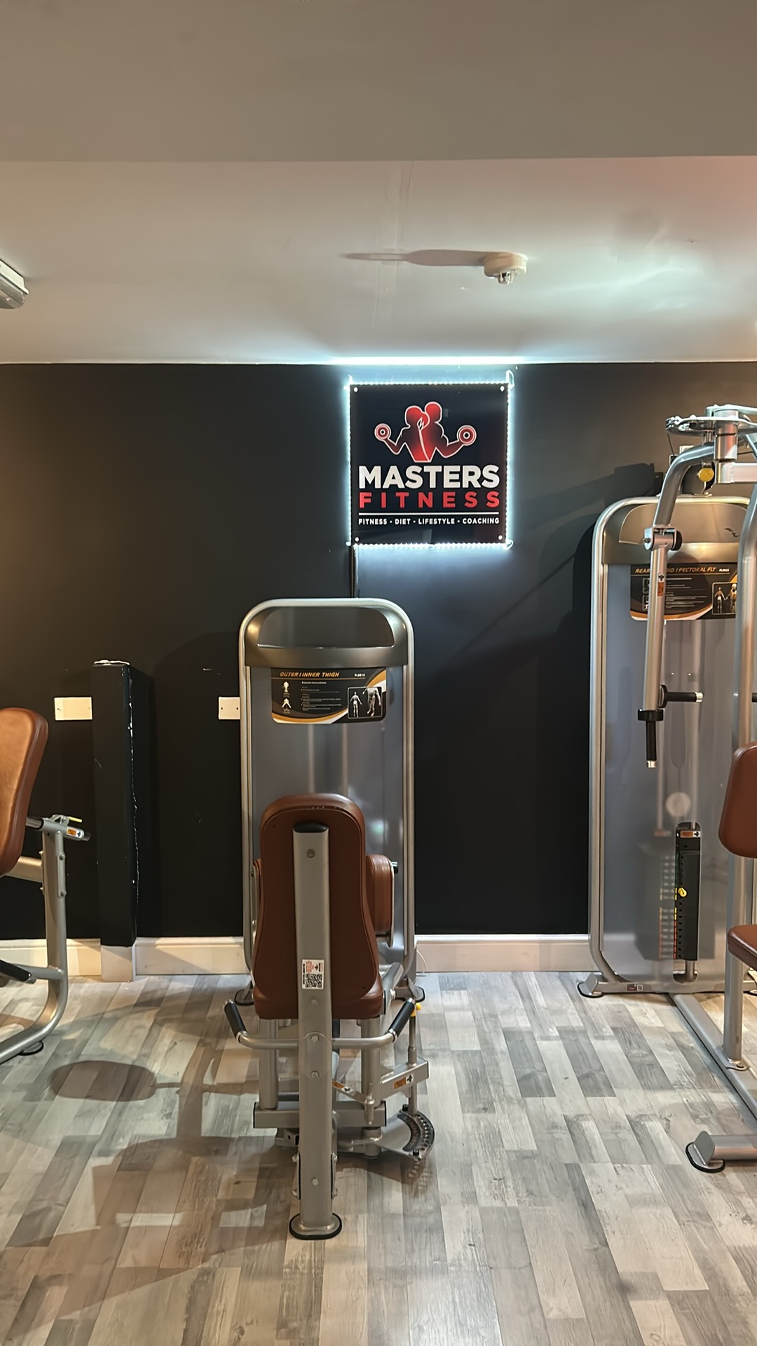 Resistance machines beside the illuminated Masters Fitness logo wall