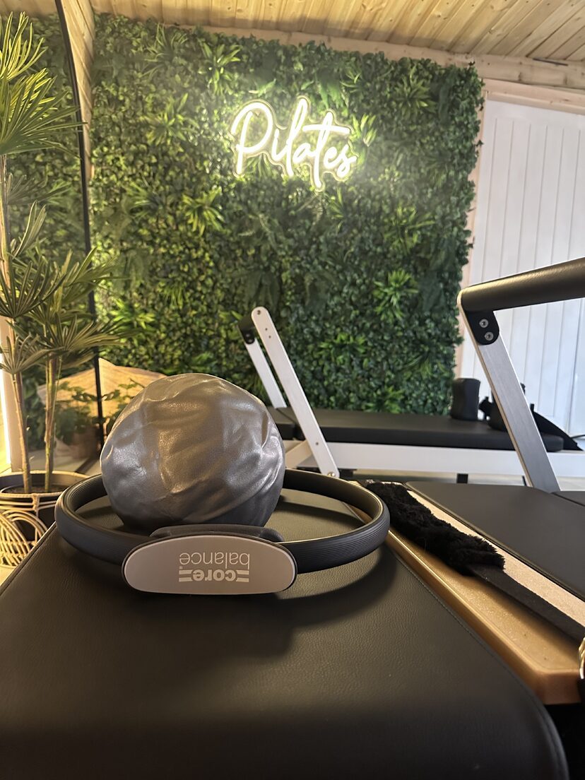 A Pilates ring and soft ball resting on a reformer in front of the illuminated Pilates sign