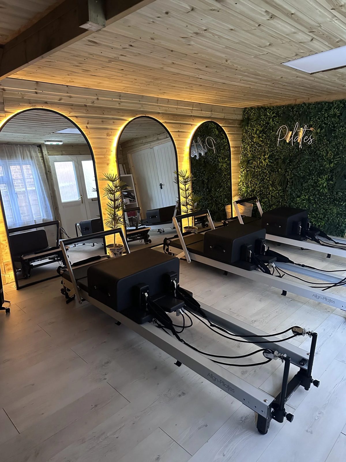Reformer machines lined up beneath arched mirrors and a living green wall in the Flow studio